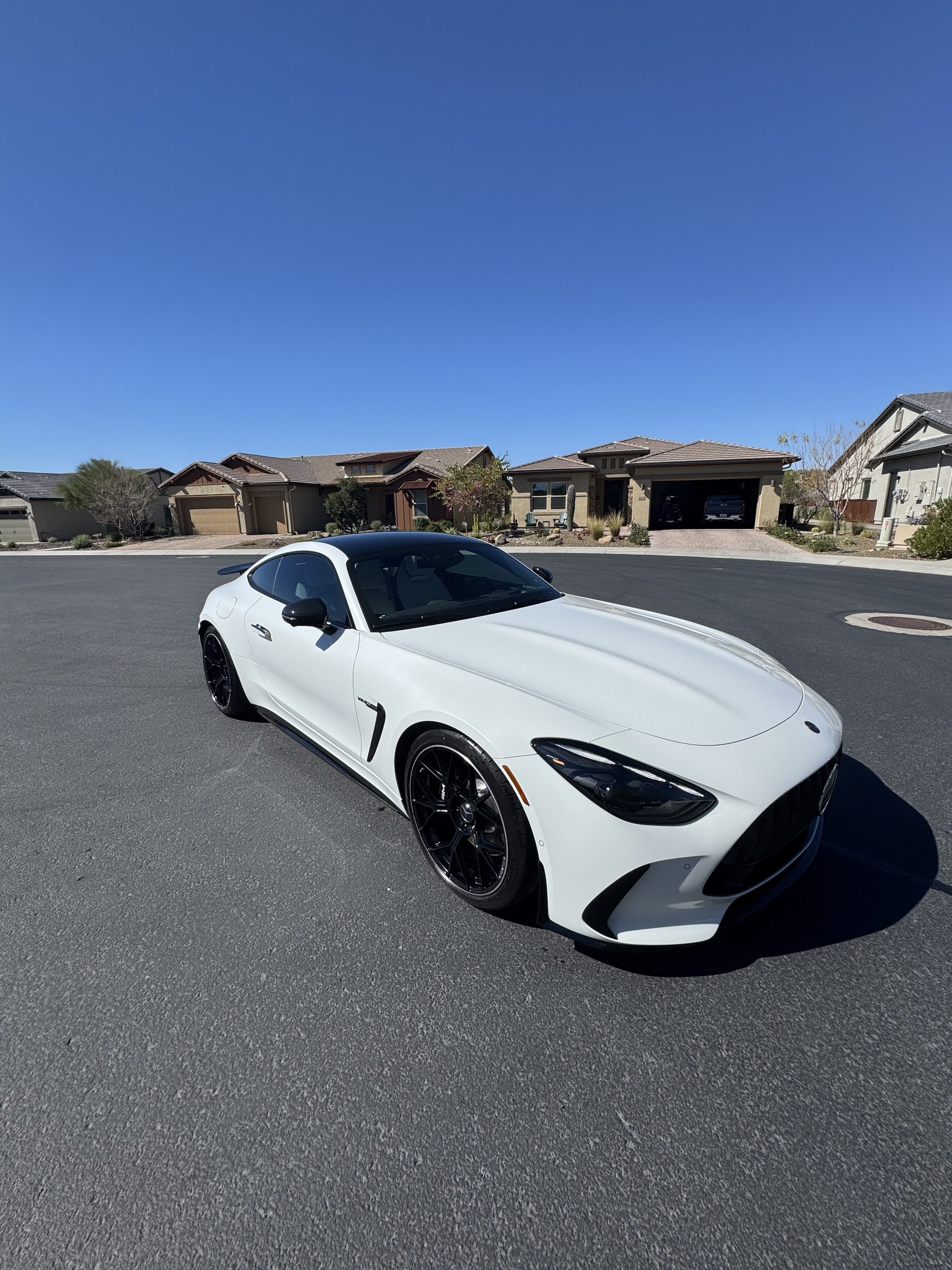 A gleaming, freshly detailed white Mercedes-AMG GT in a sunny desert neighborhood
