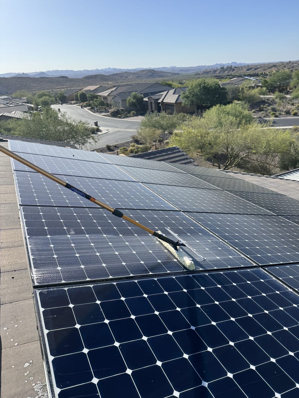 Technician cleaning rooftop solar panels with a water-fed pole brush